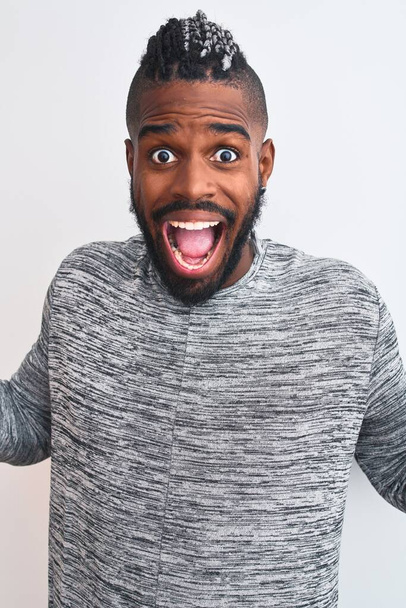 African american man with braids wearing grey sweater over isolated white background very happy and excited, winner expression celebrating victory screaming with big smile and raised hands - Valokuva, kuva