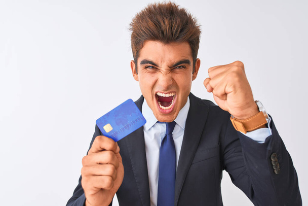 junger gutaussehender Geschäftsmann im Anzug mit Kreditkarte vor isoliertem weißen Hintergrund genervt und frustriert schreit vor Wut, verrückt und schreit mit erhobener Hand, Wut Konzept - Foto, Bild
