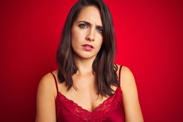 Young beautiful woman wearing sexy lingerie over red isolated background skeptic and nervous, disapproving expression on face with crossed arms. Negative person. - Fotó, kép