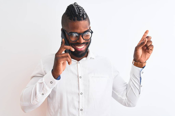 Африканський американський бізнесмен, який розмовляє на смартфоні через ізольований білий фон, дуже щасливий вказуючи пальцем збоку. - Фото, зображення