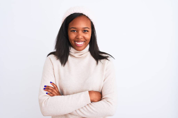 Beautiful young african american woman wearing turtleneck sweater and winter hat happy face smiling with crossed arms looking at the camera. Positive person. - 写真・画像