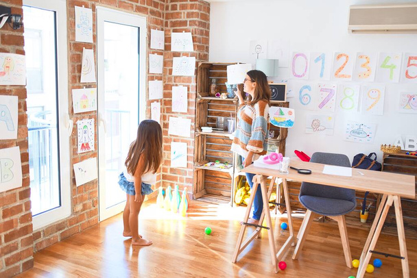 Beautiful teacher and toddler looking at draws on the wall around lots of toys at kindergarten - 写真・画像