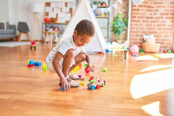 美しいアフリカ系アメリカ人の幼児は、木製ブロックで遊んでいます幼稚園でおもちゃの多くの周りのおもちゃ - 写真・画像