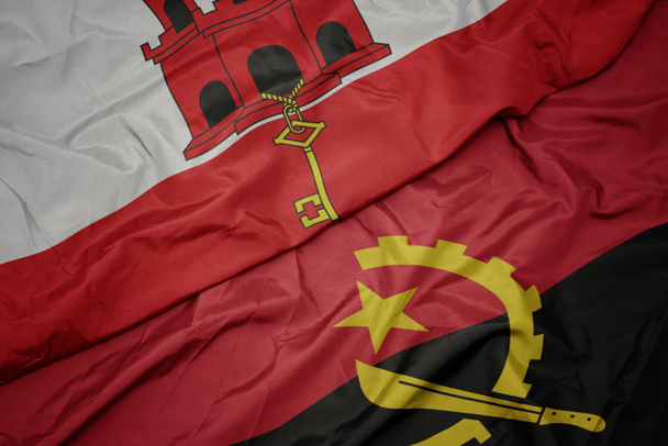 machanie barwną flagą angoli i narodową flagą gibraltaru. - Zdjęcie, obraz