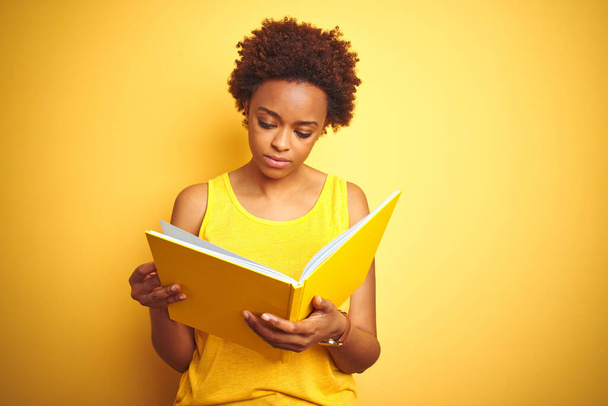 Donna afroamericana che legge un libro su sfondo giallo isolato con un'espressione sicura sul viso intelligente che pensa seriamente
 - Foto, immagini