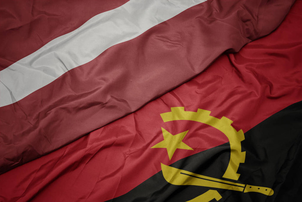 waving colorful flag of angola and national flag of latvia. - Photo, Image