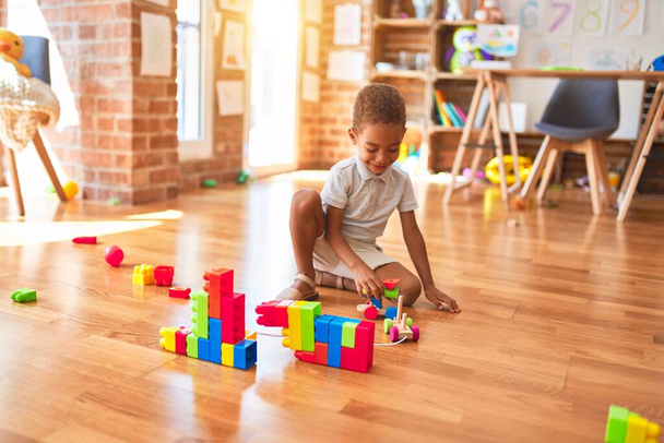 Beautiful african american toddler playing with wooden blocks train toy around lots of toys at kindergarten - Fotografie, Obrázek