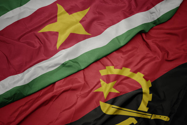 waving colorful flag of angola and national flag of suriname. - Photo, Image
