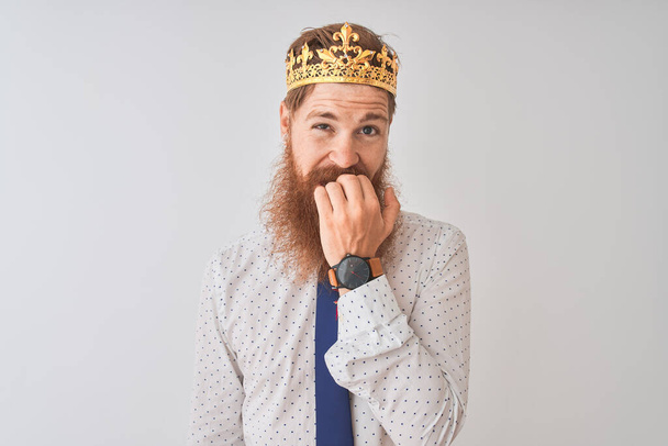 Nuori punapää irlantilainen liikemies yllään kruunu kuningas yli eristetty valkoinen tausta näyttää stressaantunut ja hermostunut kädet suulla puree kynnet. Ahdistuneisuusongelma
. - Valokuva, kuva