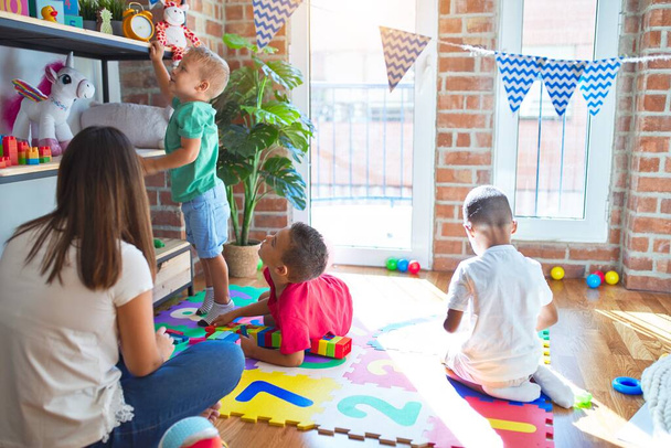 Молодой красивый учитель и малыши играют вокруг много игрушек в детском саду
 - Фото, изображение