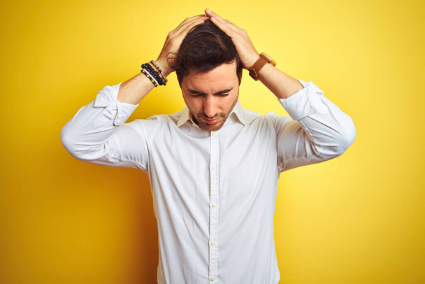 Young handsome businessman wearing elegant shirt standing over isolated yellow background suffering from headache desperate and stressed because pain and migraine. Hands on head. - Fotoğraf, Görsel