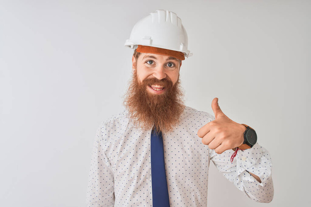 Молодой рыжий ирландский архитектор в защитном шлеме на изолированном белом фоне делает счастливый жест вверх рукой. Утверждение выражения лица, смотрящего на камеру и показывающего успех
. - Фото, изображение