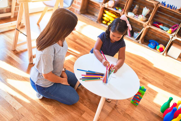 Kaunis opettaja ja lapsi tyttö piirustus piirtää käyttäen värillisiä kyniä päiväkodissa
 - Valokuva, kuva