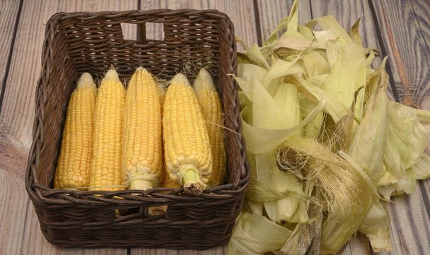 Hojas de maíz peladas en una canasta de mimbre y hojas de maíz en una mesa de madera. Cosecha de otoño. Dieta fitness. Dieta saludable. Para una golosina
. - Foto, imagen