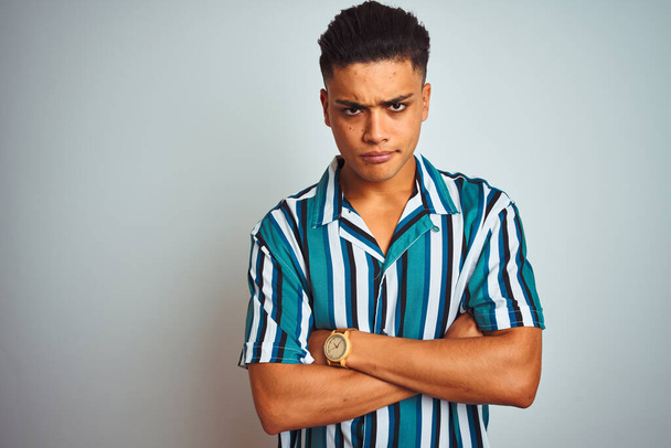 Young brazilian man wearing summer striped shirt standing over isolated white background skeptic and nervous, disapproving expression on face with crossed arms. Negative person. - Фото, зображення