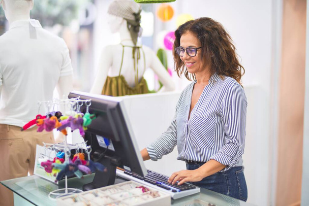 Средневековье красивая владелица магазина одежды женщина улыбается счастливой и уверенной в себе работы с компьютером за прилавком
 - Фото, изображение