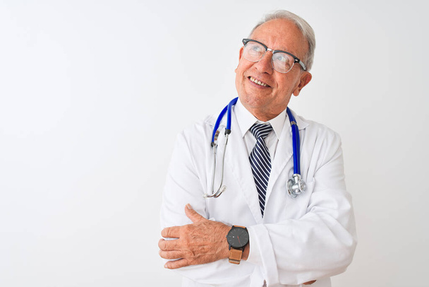 Senior grijsharige arts draagt stethoscoop staan over geïsoleerde witte achtergrond glimlachend kijken naar de zijkant en staren weg denken. - Foto, afbeelding
