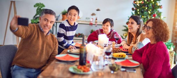 Hermosa familia sonriendo feliz y confiada. Comer pavo asado hacer selfie por teléfono inteligente celebrando la Navidad en casa
 - Foto, imagen