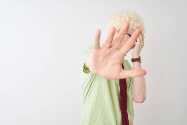 Jovem empresário albino vestindo camisa e gravata em pé sobre fundo branco isolado cobrindo os olhos com as mãos e fazendo gesto de parada com expressão triste e medo. Conceito embaraçoso e negativo
. - Foto, Imagem