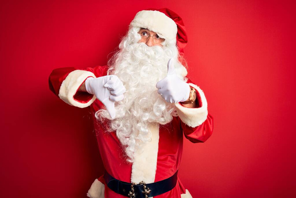 Moyen-âge bel homme portant costume de Père Noël debout sur fond rouge isolé Faire pouces de haut en bas, désaccord et expression d'accord. Conflit fou
 - Photo, image