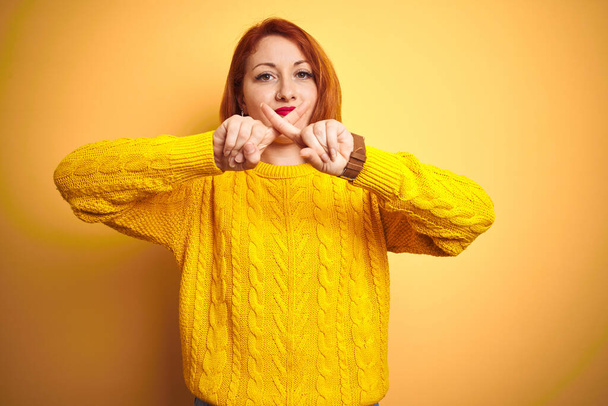Belle femme rousse portant un pull d'hiver debout sur fond jaune isolé Expression de rejet croisant les doigts faisant signe négatif
 - Photo, image