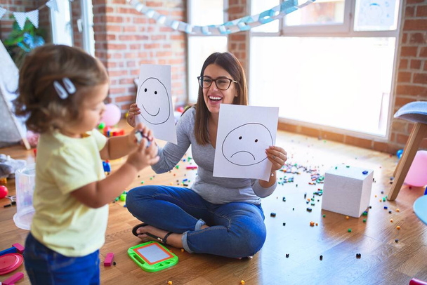 Young beautiful psicologist and toddler doing therapy using emoji emotions at kindergarten - Fotografie, Obrázek