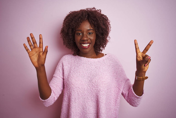 Mladý africký afro žena na sobě svetr stojící nad izolované růžové pozadí ukazující a ukazující nahoru s prsty číslo sedm při úsměvu sebevědomý a šťastný. - Fotografie, Obrázek