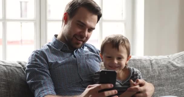 Happy dad teaching child son using smartphone apps at home - Záběry, video