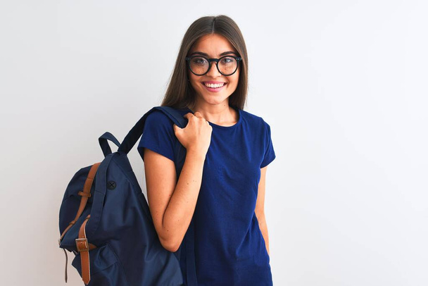 Νεαρή όμορφη μαθήτρια που φοράει σακίδιο και γυαλιά πάνω σε απομονωμένο λευκό φόντο με χαρούμενο πρόσωπο στέκεται και χαμογελά με αυτοπεποίθηση χαμόγελο που δείχνει τα δόντια - Φωτογραφία, εικόνα