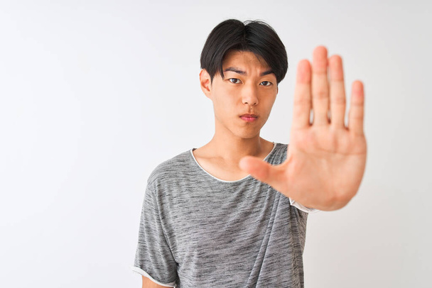 Young chinese man wearing casual t-shirt standing over isolated white background with open hand doing stop sign with serious and confident expression, defense gesture - Photo, Image