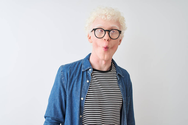 junger albinoblonder Mann mit Jeanshemd und Brille über isoliertem weißem Hintergrund, der Fischgesicht mit Lippen, verrückte und komische Gesten macht. Lustiger Ausdruck. - Foto, Bild
