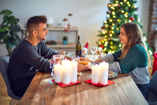 若い美しいカップルの幸せと自信を笑顔。家でクリスマスを祝う食べ物を食べる - 写真・画像