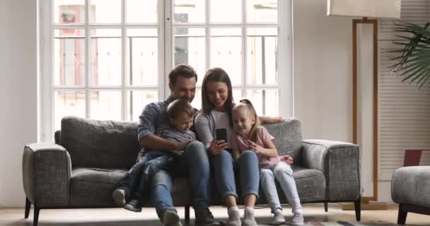Familia feliz de cuatro usando teléfono inteligente relajarse en el sofá
 - Metraje, vídeo