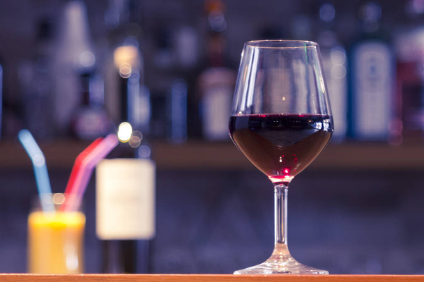 Close-up of a glass of red wine on a bar counter with a blurred colorful background - Foto, Imagem