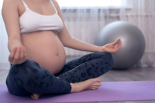 primo piano della donna incinta in top bianco e leggings seduti sullo sport Mat in posizione Lotus fare yoga
 - Foto, immagini