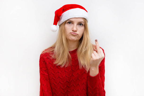 Joven hermosa mujer con sombrero de Navidad que muestra el dedo medio. Emoción expresión facial
. - Foto, Imagen