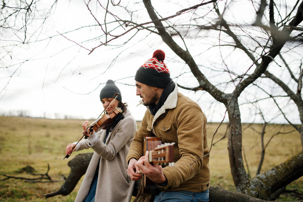 Two musicians sitting on a branch, playing music in a autumn countryside - Фото, изображение