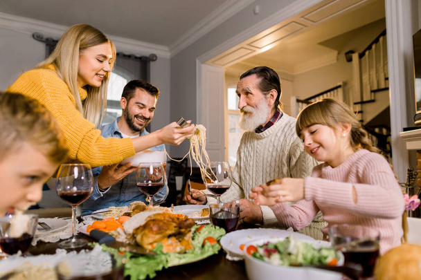Domestic casual lifestyle, thanksgiving dinner concept. Large happy family enjoying time together having tasty dinner, vegetable salad, pasta, turkey - Foto, imagen