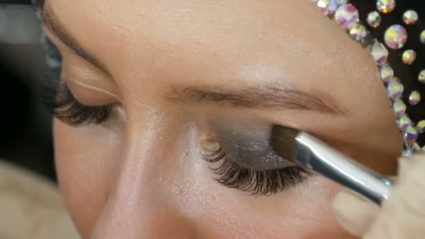 Makeup artist makes models smoky eyes with the help of special brush gray eyeshadow, eyes and eyelashes of girl close up view. Professional high fashion. - Imágenes, Vídeo