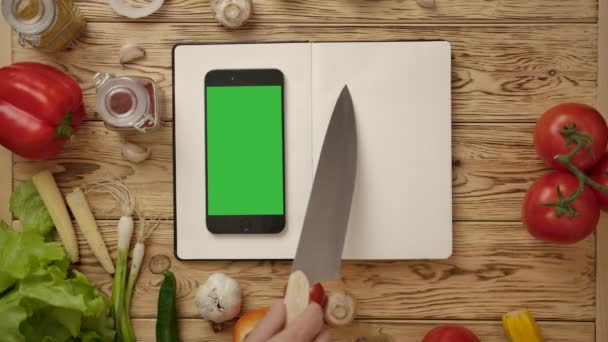 Ernteköchin zeigt mit Messer auf Linien in leerem Tagebuch beim Kochen mit Online-Rezept - Filmmaterial, Video