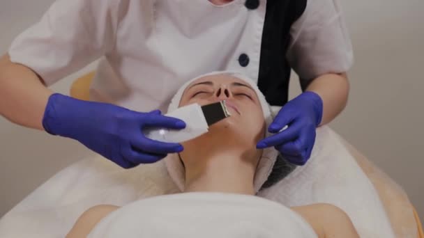 Professional beautician does ultrasonic face cleaning for middle-aged woman. - Footage, Video