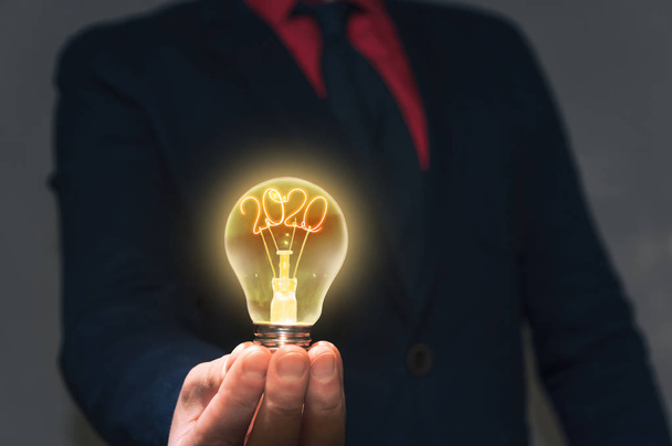Бизнесмен держит перед собой лампу с новым 2020 годом. Концепция новых идей Новые открытия
. - Фото, изображение