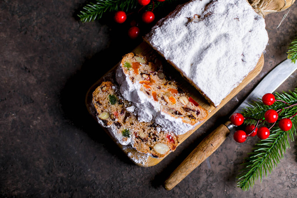 Christmas stollen on wooden tray on brown concrete background. Traditional Christmas pastry dessert with festive decoration. Top view, copy space - Photo, Image