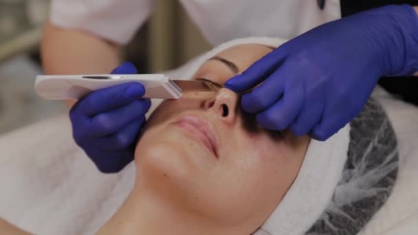 Professional beautician does ultrasonic face cleaning for middle-aged woman. - Footage, Video