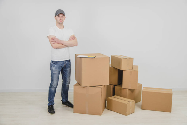 Strong young delivery man standing with his hands folded, near a stack of cardboard packages. - Fotografie, Obrázek