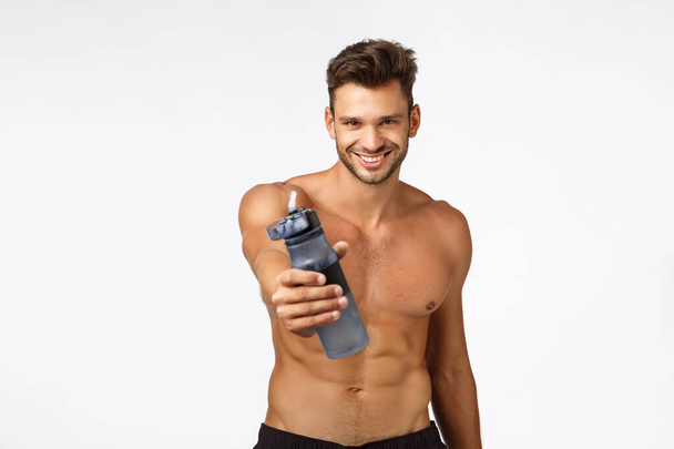 Sexy handsome and self-assured sportsman give you water bottle drink and refresh, smiling confident, posing naked torso. Shirtless sassy athlete give drink after productive fitness workout - Fotó, kép