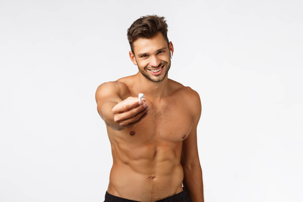Сексуально привлекательный улыбающийся молодой спортсмен без рубашки даст вам один беспроводной наушник слушать музыку вместе во время тренировки, фитнес-тренировки, улыбаясь радостно, стоя голый торс показать идеальное тело
 - Фото, изображение
