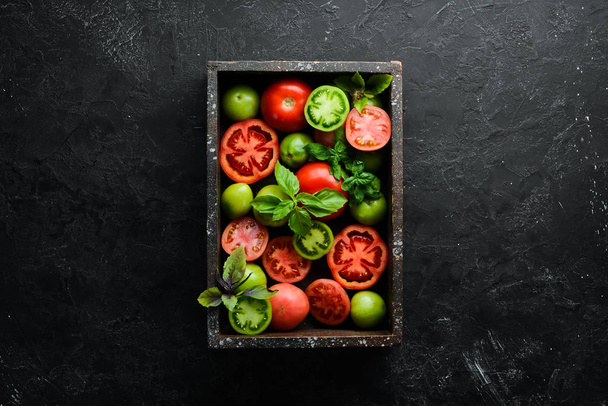 Colored tomatoes with a jar of oil in a wooden box. On a black stone background. Top view. Free space for your text. - Фото, зображення