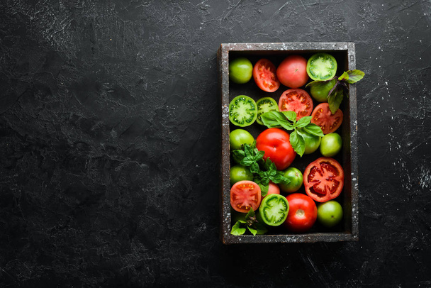 Colored tomatoes with a jar of oil in a wooden box. On a black stone background. Top view. Free space for your text. - Foto, imagen