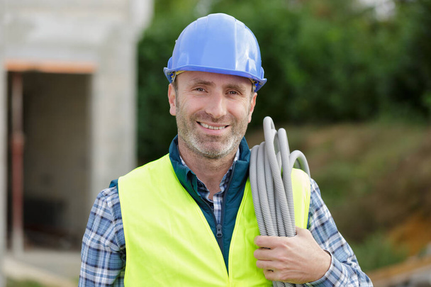 portrait of a smiling worker carrying corrugated conduit - Foto, Imagen